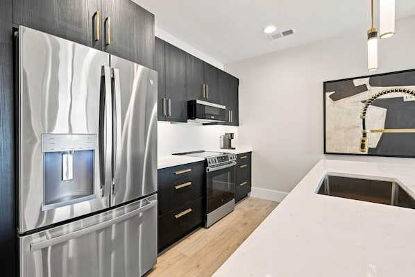 A modern kitchen with stainless steel appliances, dark cabinetry, and a white countertop.