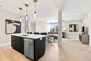 A modern kitchen with a central island, a dining area with a sofa and chairs, and a living room with a TV and artwork.