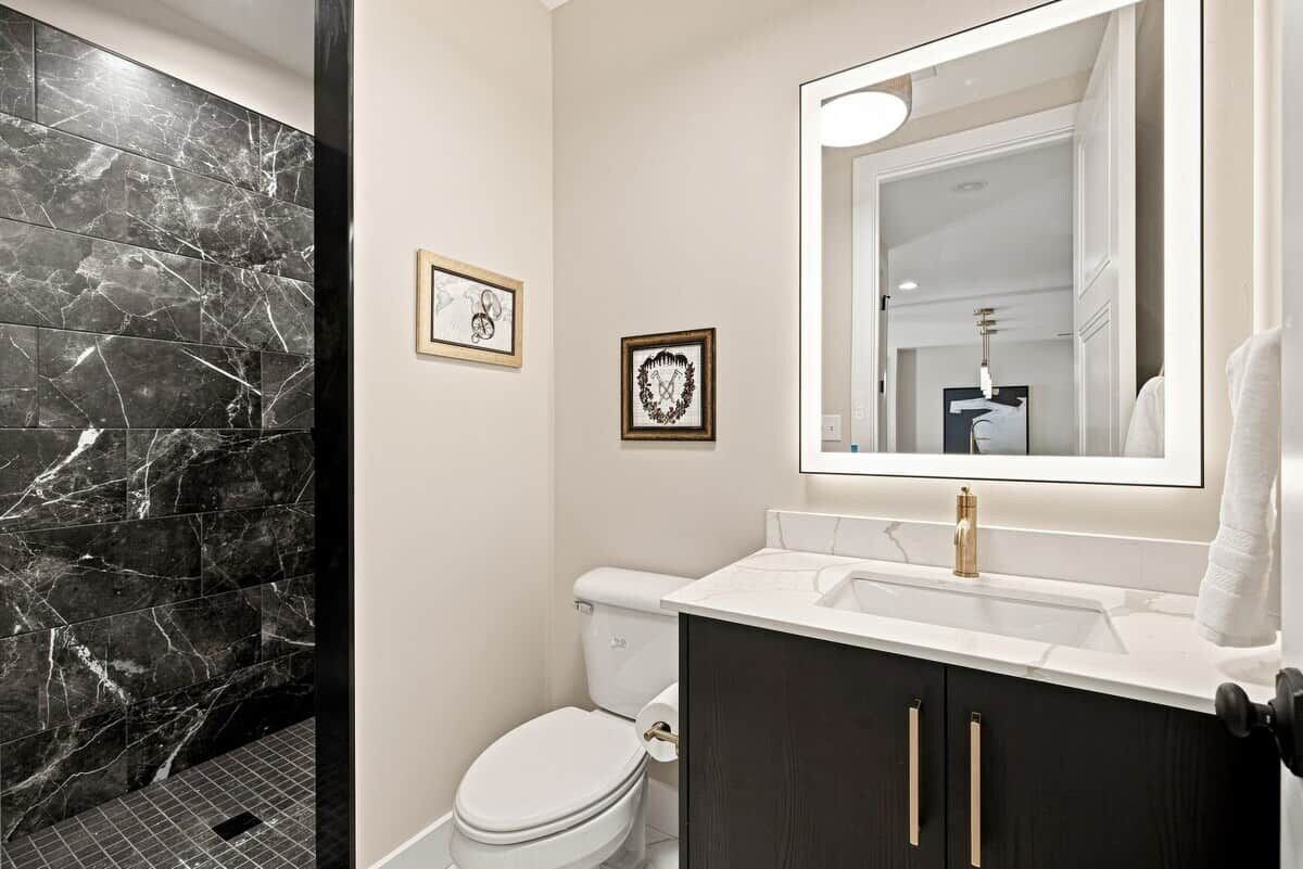 Une salle de bain moderne avec un mur de douche en marbre, des toilettes blanches, un meuble-lavabo avec un robinet doré et deux tableaux encadrés accrochés au mur.