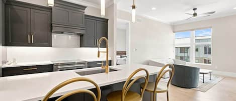 A modern kitchen with dark cabinets, a white countertop, and gold fixtures.