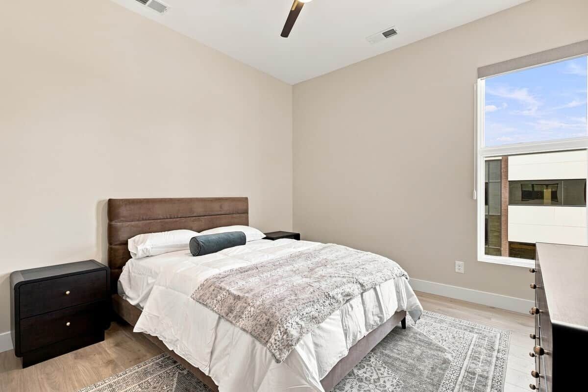 Un dormitorio con cama, mesita de noche y ventana.