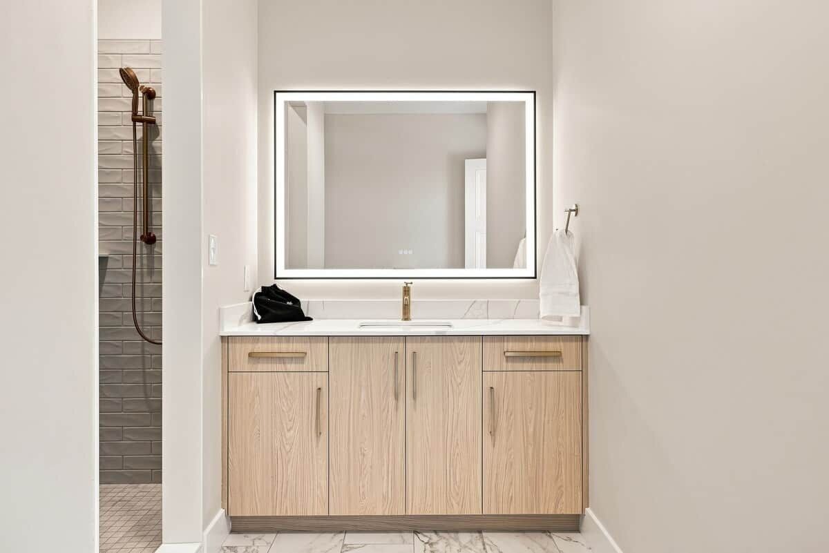 Ein modernes Badezimmer mit einem großen Spiegel, einem Waschbecken und Holzschränken.