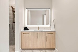 A modern bathroom with a large mirror, a sink, and wooden cabinets. - The Regent · 2 Bed · 2 Bath · 1,300+ SF (Owensboro)