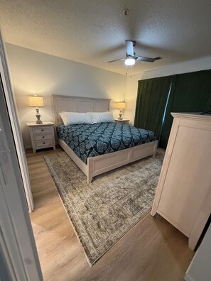 A bedroom with a bed, two bedside tables with lamps, a ceiling fan, a green curtain, and a wooden floor. - Spacious 2-bedroom condo with indoor pool and workout room. (Branson)