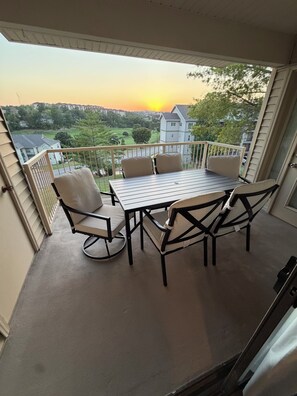 A balcony with a table and chairs, overlooking a residential area during sunset. - Spacious 2-bedroom condo with indoor pool and workout room. (Branson)