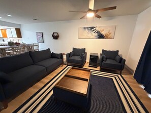 A modern living room with a dark-colored sofa, two armchairs, a coffee table, and a ceiling fan. - Spacious 2-bedroom condo with indoor pool and workout room. (Branson)