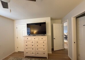 A hallway with a white dresser, a flat-screen TV on top, and two closed doors. - Spacious 2-bedroom condo with indoor pool and workout room. (Branson)