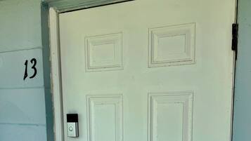 Une porte blanche avec le numéro « 13 » peint sur le mur, à gauche, un interphone et une poignée de porte.