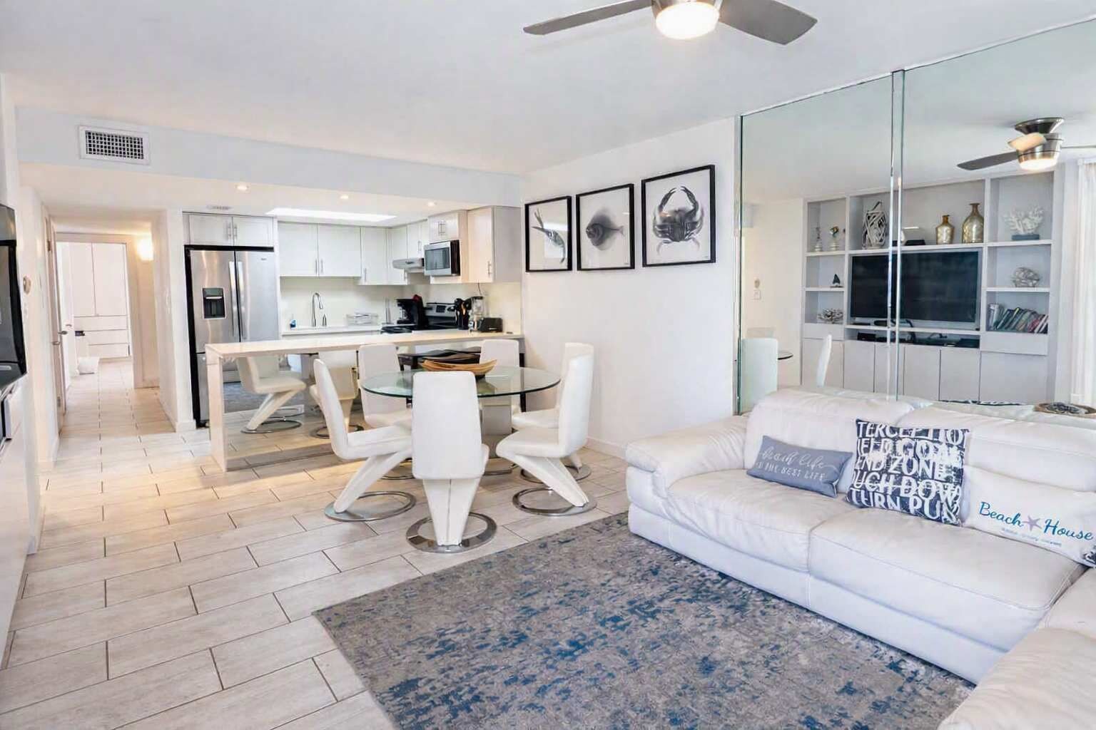 Een moderne woonkamer met een witte bank, een glazen salontafel en een eethoek met witte stoelen.