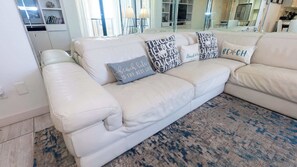 Un canapé en cuir blanc agrémenté de plusieurs coussins, un tapis à motifs et un salon moderne doté d’une porte en verre donnant sur un balcon.