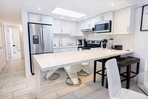 A modern kitchen with white cabinetry, stainless steel appliances, a central island, and a dining area with bar stools. - Sea Vista Beachfront 3BR - Heated Pool (South Padre Island)