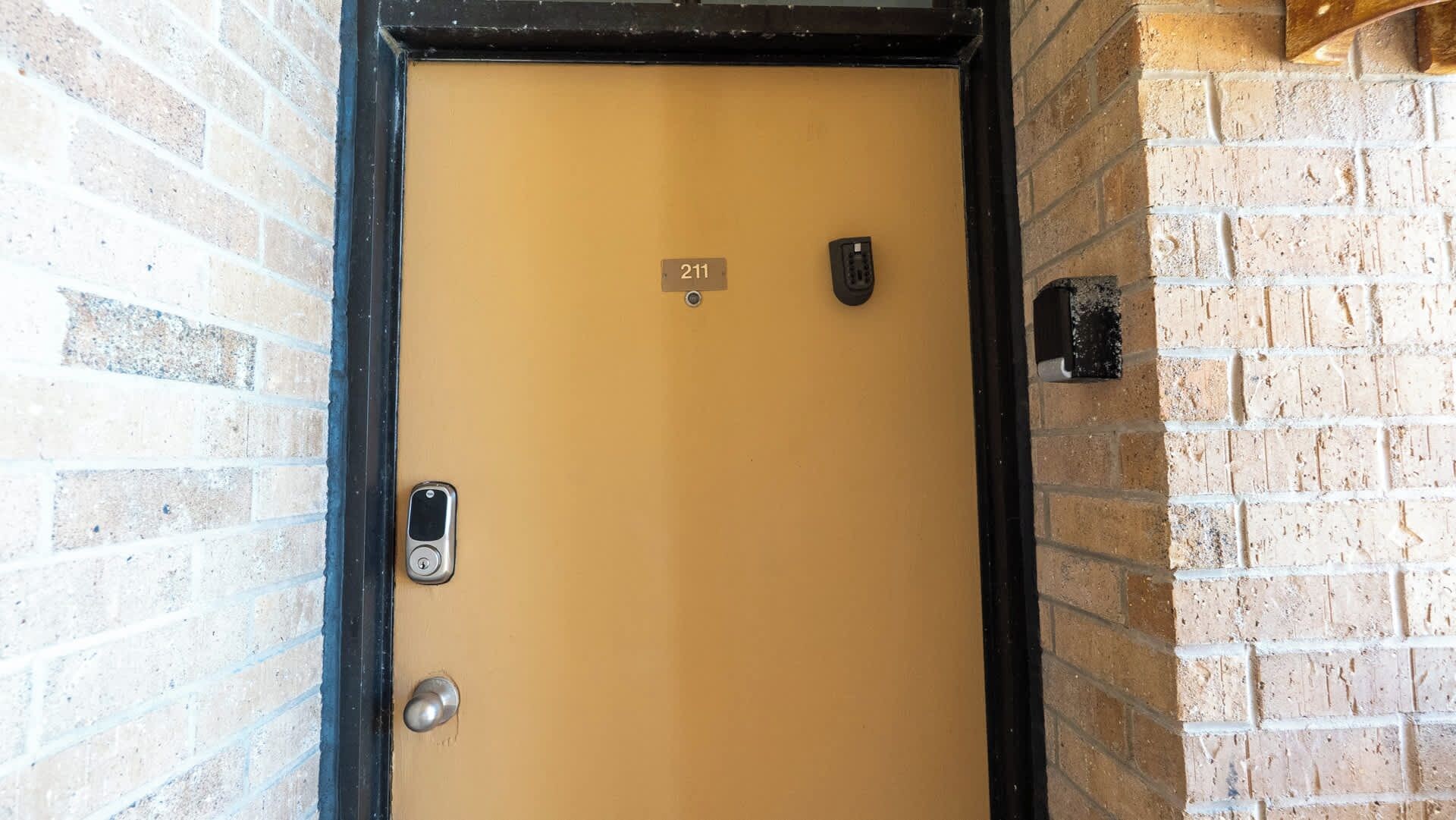 A door with a numeric keypad and a lock, set in a brick wall.