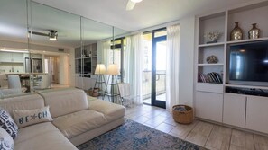 A modern living room with a sofa, a television, and a bookshelf. - Sea Vista Beachfront 3BR - Heated Pool (South Padre Island)