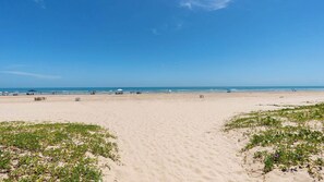 Une vaste plage de sable fin, avec un ciel dégagé, des parasols et une végétation clairsemée.