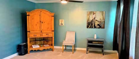 A room with a ceiling fan, a wooden cabinet, a chair, and a painting on the wall.