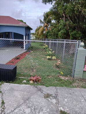Ein eingezäunter Garten mit einem Gebäude, einer Palme und einer Betonbank.