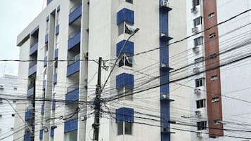 Un edificio de varios pisos con balcones, entrada protegida por una reja y líneas eléctricas visibles.