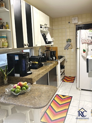 A kitchen with a granite countertop, a coffee maker, a blender, and a refrigerator. - Apartamentos RC Hospedagem (Recife)