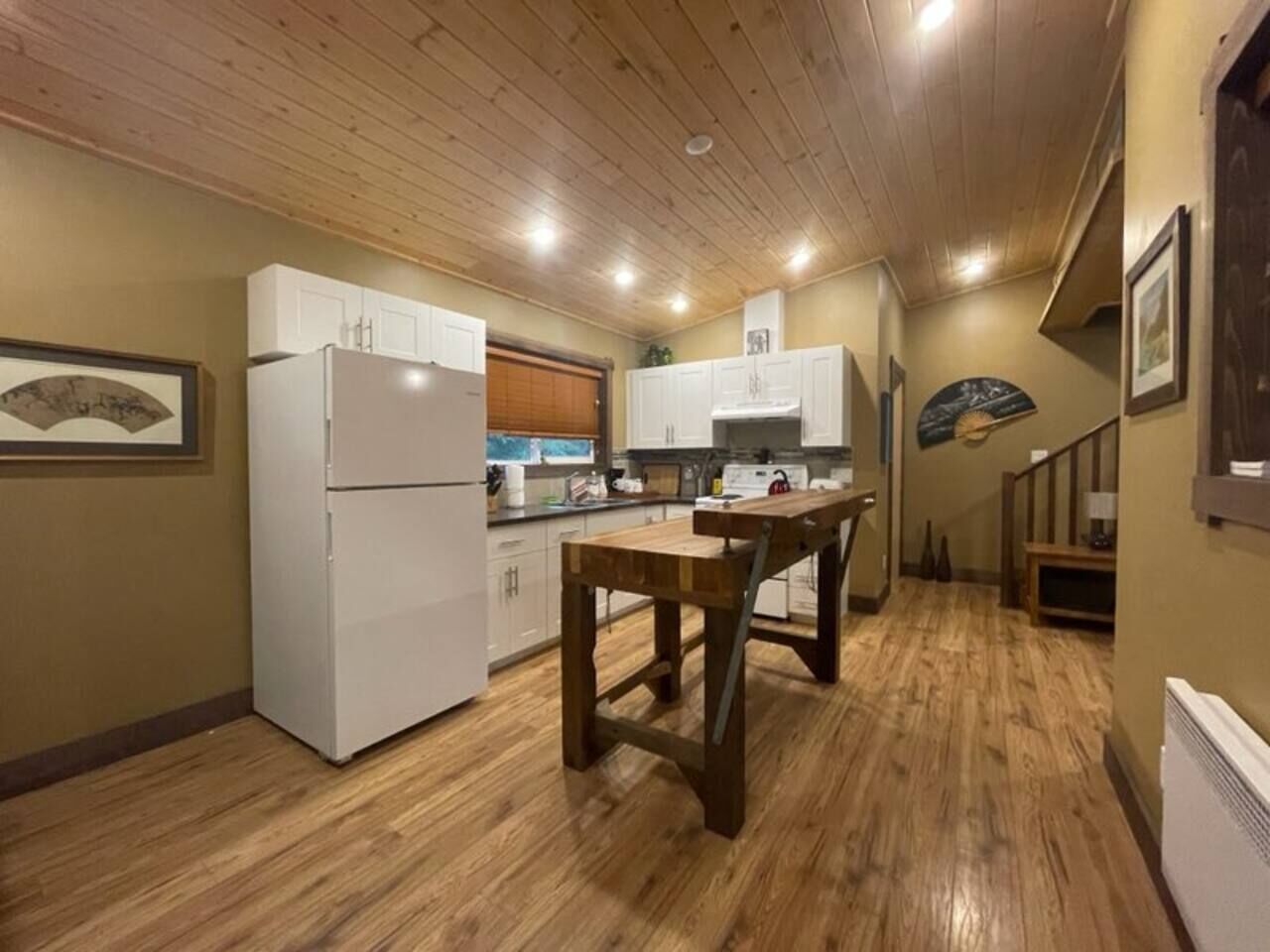 A kitchen with wooden flooring, white cabinets, and a wooden dining table.