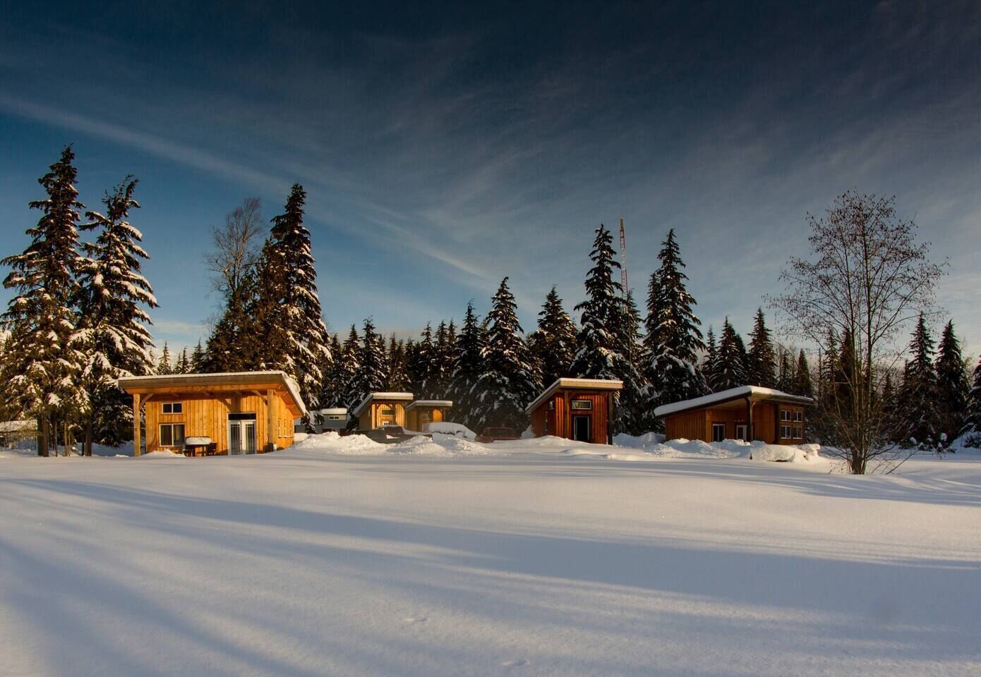 A snow-covered landscape with wooden cabins and tall evergreen trees.