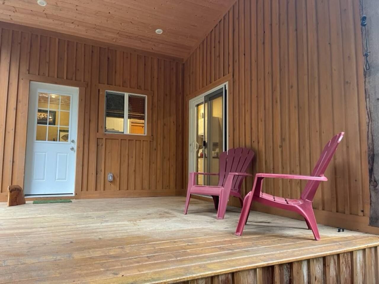 Une cabane en bois avec une véranda, deux fauteuils Adirondack et une porte avec des fenêtres.