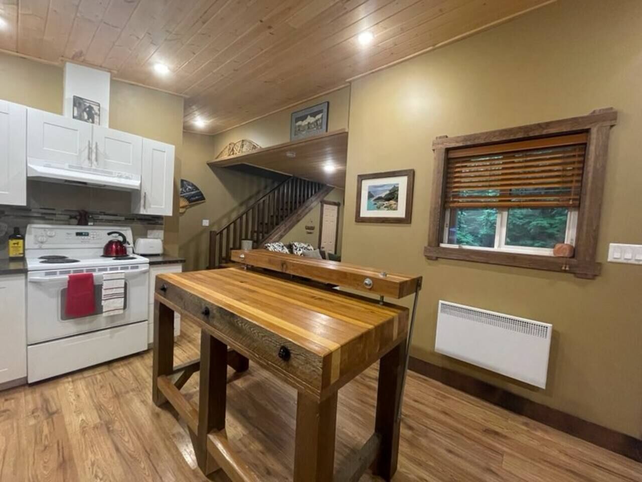 A kitchen with a wooden table, white cabinets, a stove, and a window with blinds.