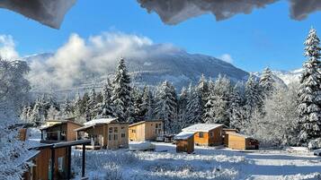Paisaje nevado con varias cabañas de madera y una pequeña estructura de madera, probablemente una posada, con montañas al fondo.
