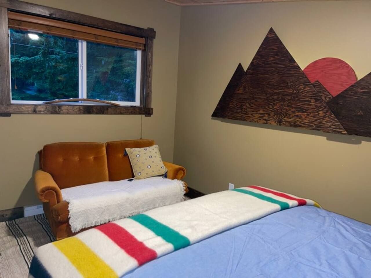 A room with a bed, a chair, a window, and a wall with a geometric design.