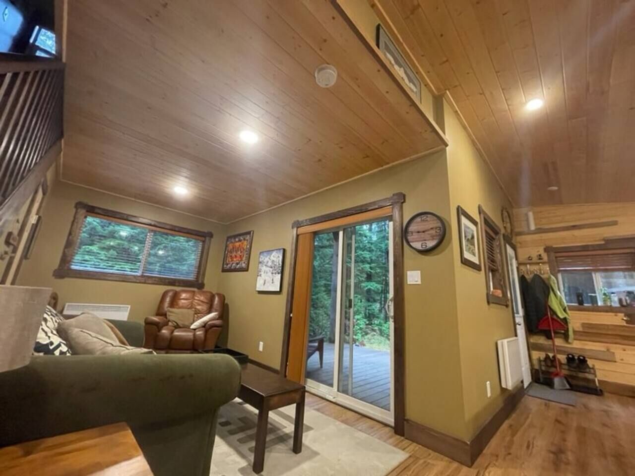 A cozy room with a green sofa, a leather chair, a wooden table, and a sliding glass door leading to a deck.