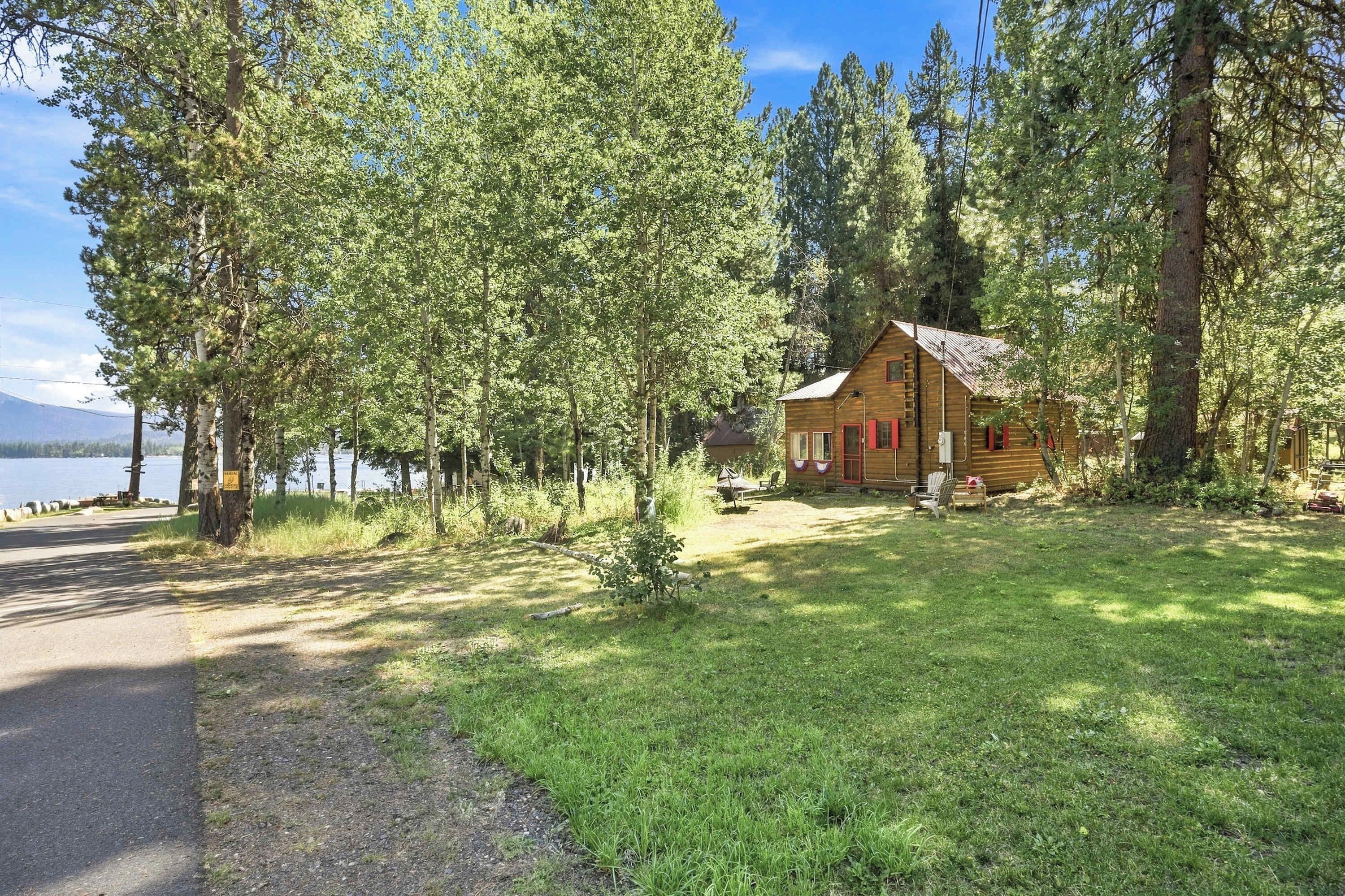 A cabin with a wooden exterior, surrounded by trees, near a body of water.