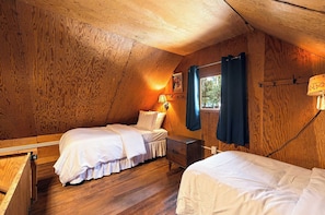A cozy attic bedroom with wooden walls, two beds, a nightstand, a lamp, and a window with curtains. - Cozy Lakeside Cabin: Dock, Deck, & Pet Friendly (McCall)