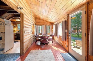 A log cabin interior with a dining area, wooden walls, and large windows. - Cozy Lakeside Cabin: Dock, Deck, & Pet Friendly (McCall)