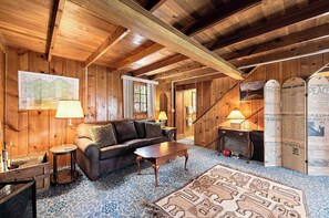 A cozy wooden cabin interior with a sofa, coffee table, and a map on the wall. - Cozy Lakeside Cabin: Dock, Deck, & Pet Friendly (McCall)