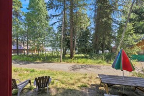 A wooden deck with a picnic table and chairs, surrounded by a forested area with tall trees. - Cozy Lakeside Cabin: Dock, Deck, & Pet Friendly (McCall)