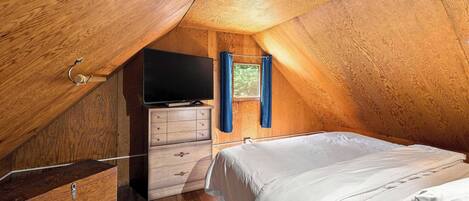 Un dormitorio acogedor en el ático con techo inclinado de madera, televisión de pantalla plana, cómoda y cama.