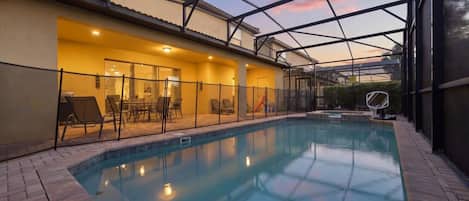 An indoor swimming pool with a glass ceiling, surrounded by a fenced patio area with chairs and tables.