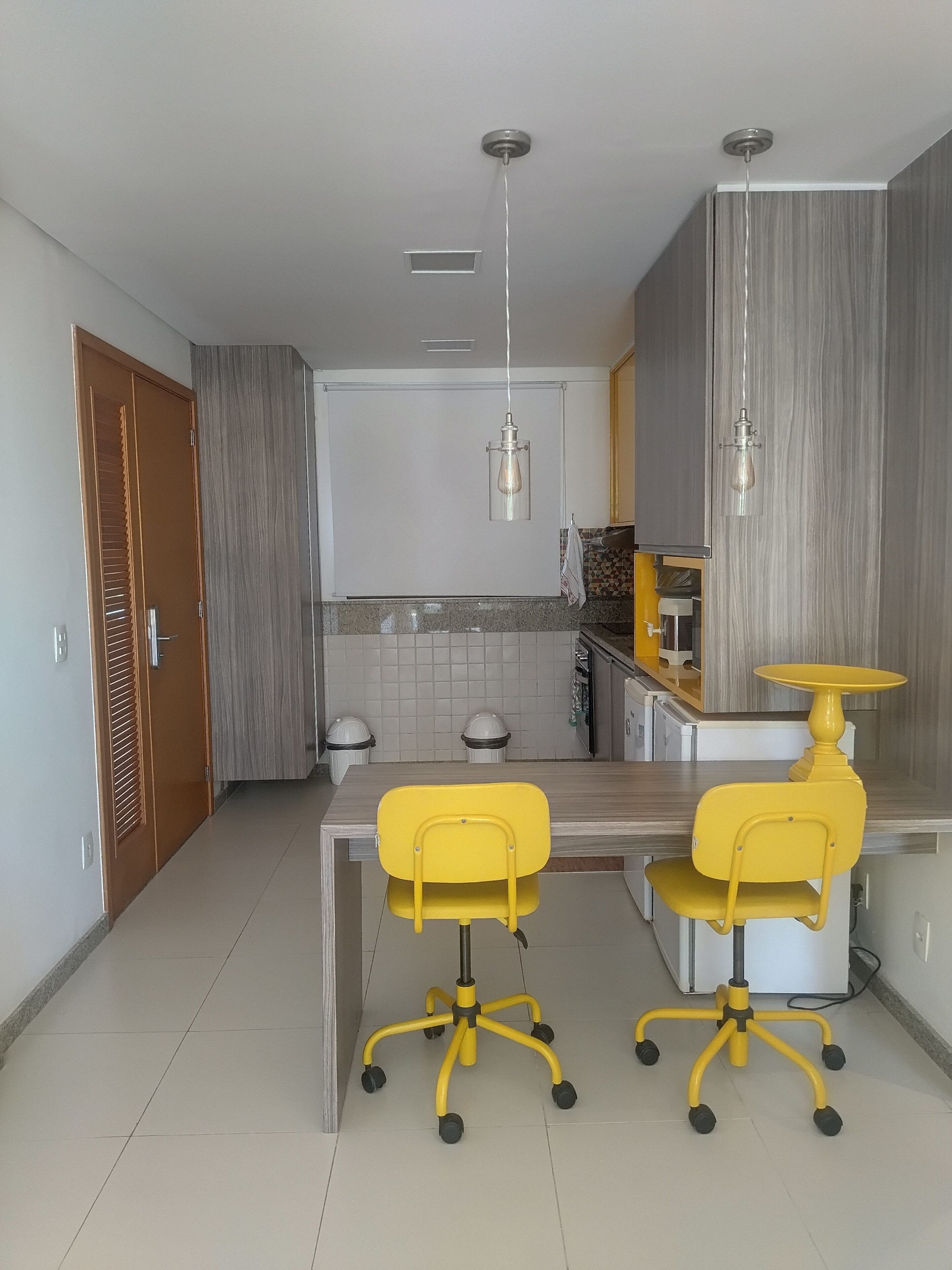 A modern kitchen with a dining table, two yellow chairs, and a pendant light.