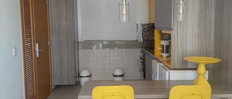 A modern kitchen with a dining table, two yellow chairs, and a pendant light.