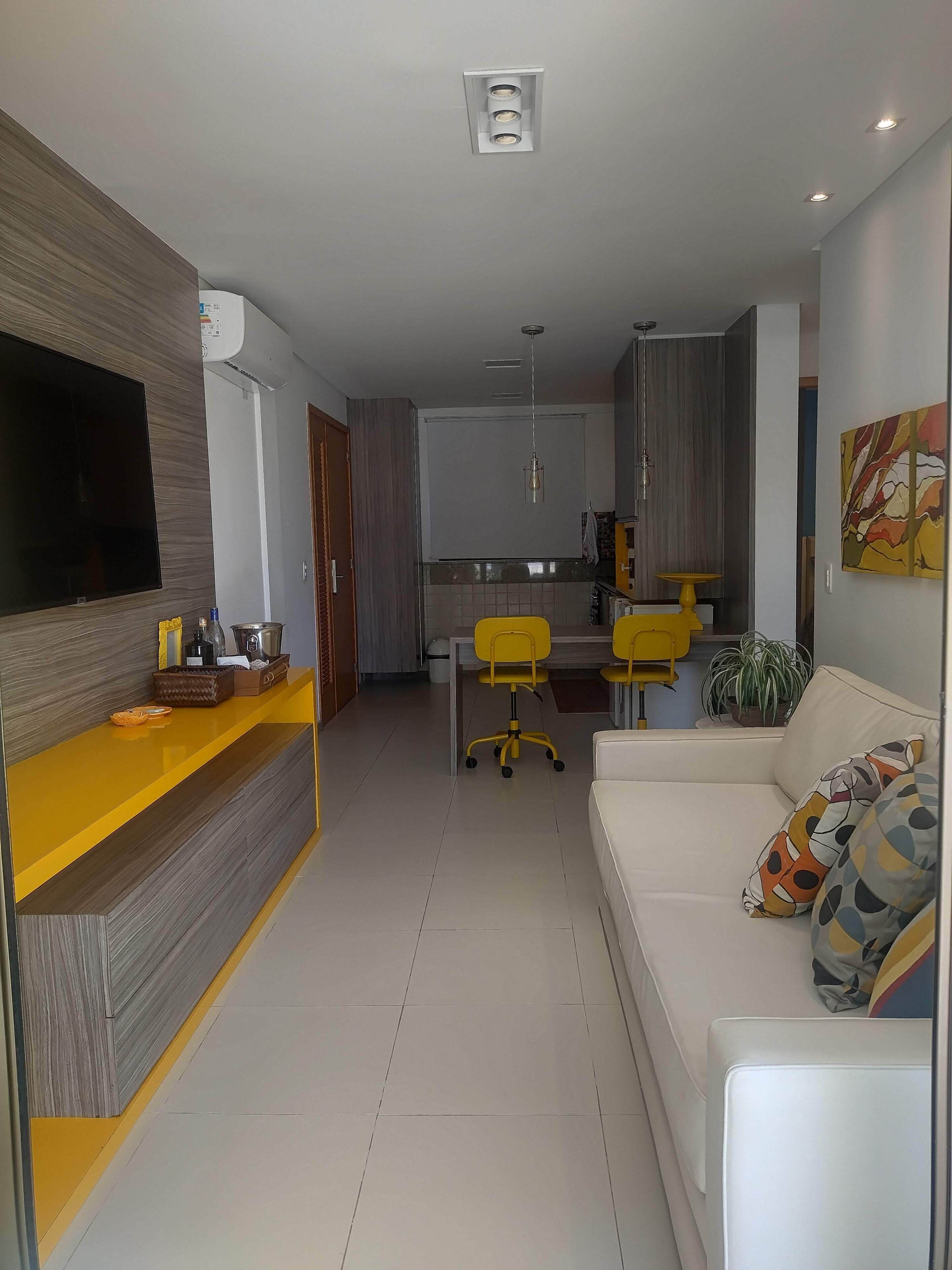 A modern living room with a sofa, a TV, and a kitchen area in the background.
