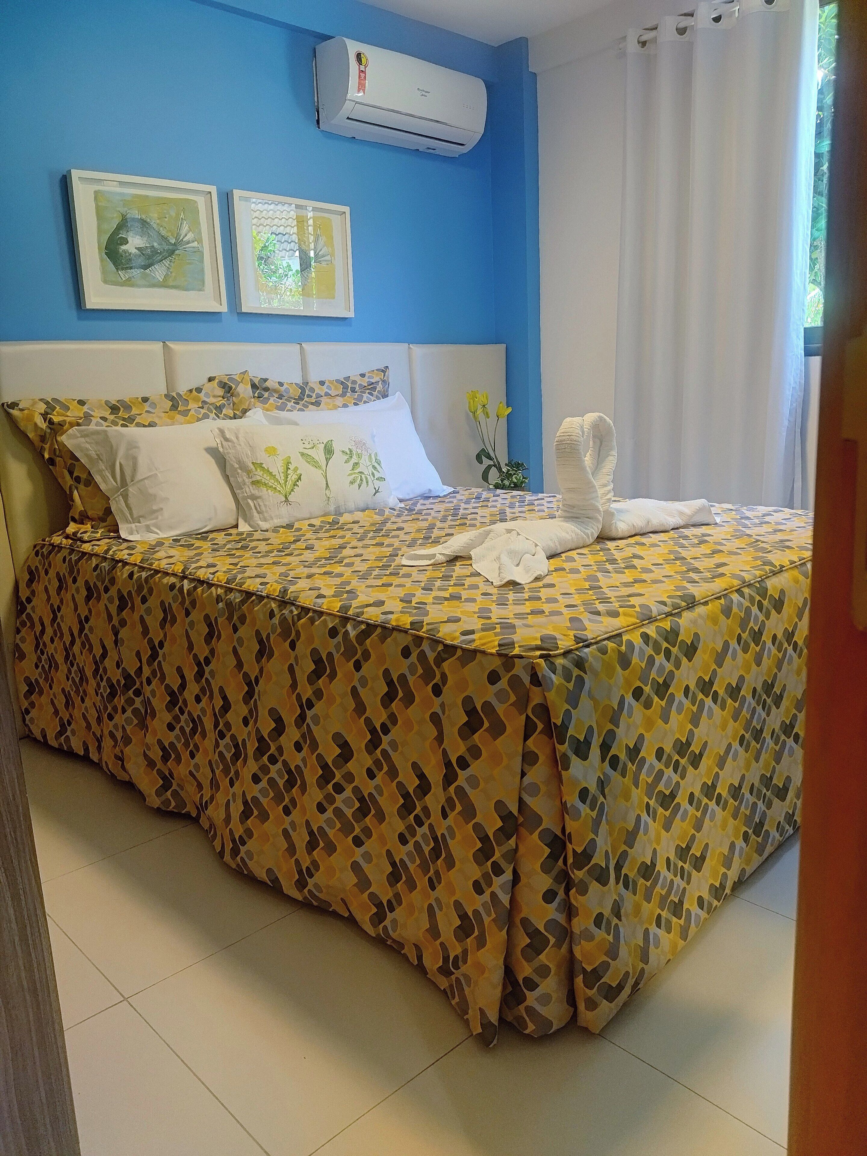 A hotel room with a bed, a wall-mounted air conditioner, and two framed pictures.