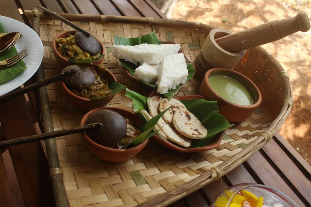 A traditional meal setup with a woven basket containing rice, flatbreads, and various dishes, including a green sauce and a dark soup.
