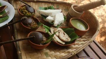 A traditional meal setup with a woven basket containing rice, flatbreads, and various dishes, including a green sauce and a dark soup.
