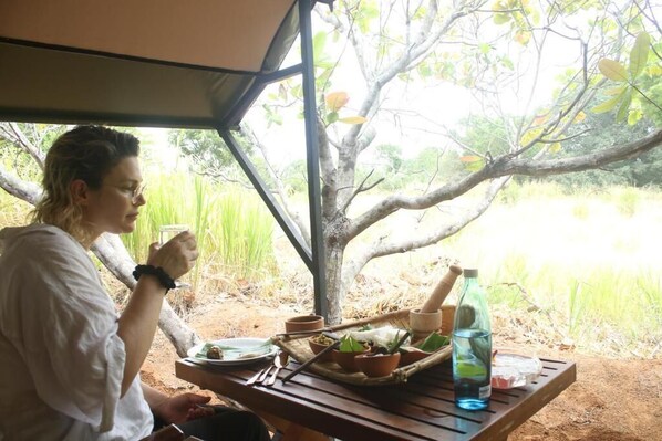 A person dining at an outdoor table with a view of a tree and water.