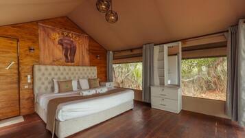 A bedroom with a large bed, wooden walls, a mounted headboard, a wardrobe, and a window with a view of vegetation.