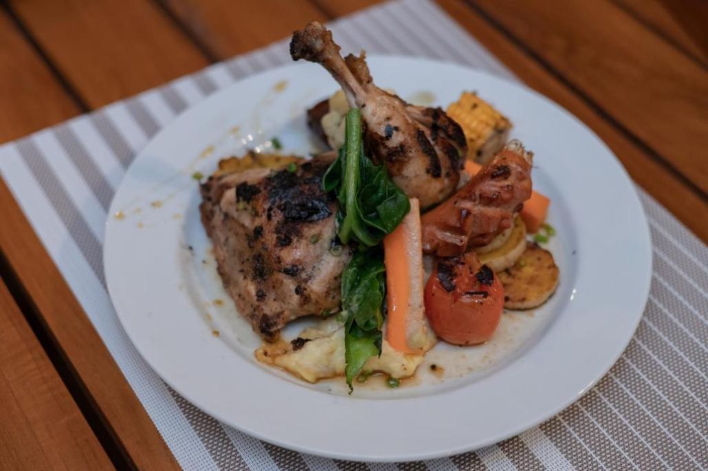 A plate of food with a grilled chicken leg, vegetables, and a slice of bread.