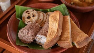 Un plato con diversos alimentos, entre ellos pan y un postre, servido sobre una hoja de plátano.