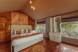 Une chambre avec un grand lit, une tête de lit en bois à motifs léopard, une armoire et une fenêtre donnant sur les arbres.