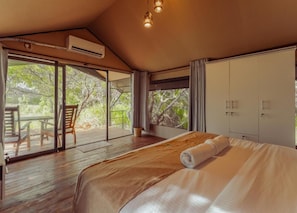 Une chambre dotée d’un grand lit, d’un appareil de climatisation, d’une porte-fenêtre coulissante donnant sur un espace extérieur avec une table et des chaises, et d’une armoire.
