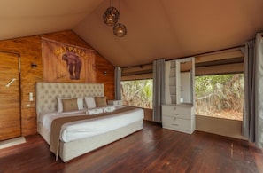 A bedroom with a large bed, wooden walls, a mounted headboard, a wardrobe, and a window with a view of vegetation. - Wilpattu Wilderness Camping - Tent 2 (Wilpattu)