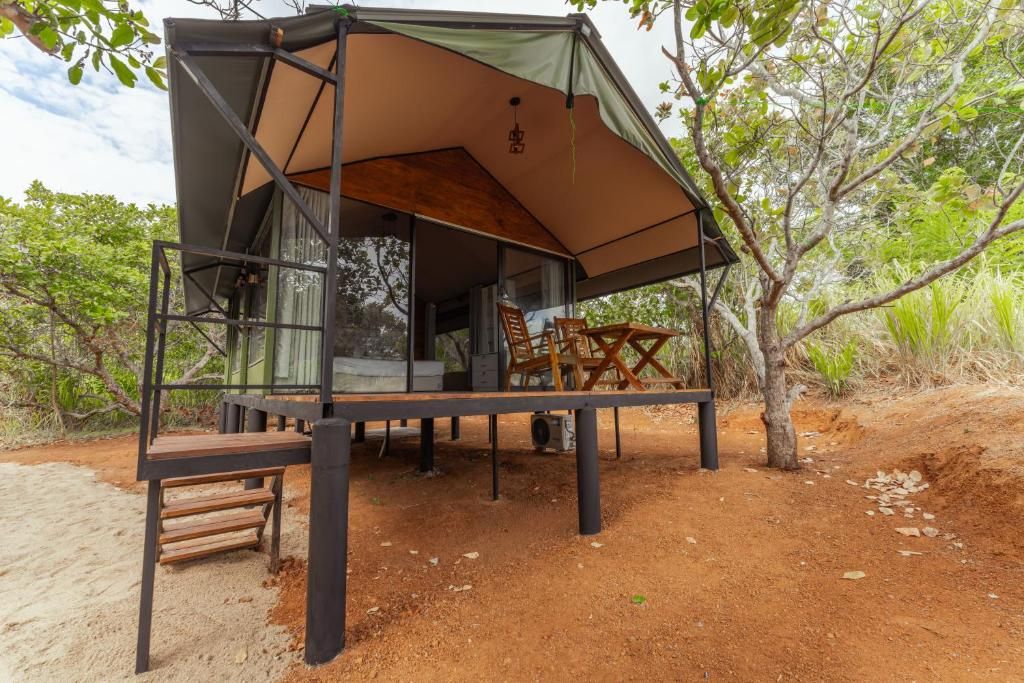 A treehouse with a wooden deck, a table, and chairs, surrounded by natural vegetation.